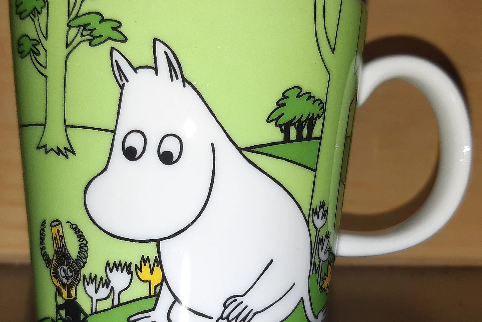 Lähikuva vihreästä Muumi-mukista, jossa Muumipeikko istuu puun alla