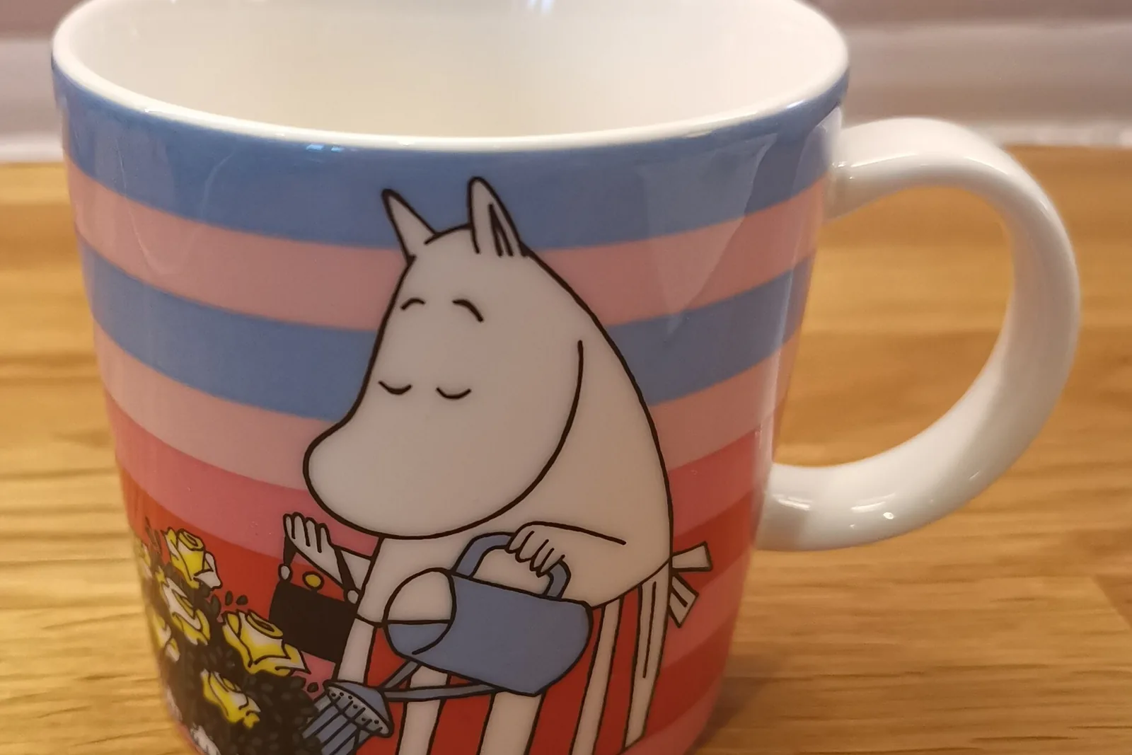 Muumimamma-aiheinen Muumi-muki, jossa Muumimamma kastelee kukkia raidallisella taustalla
