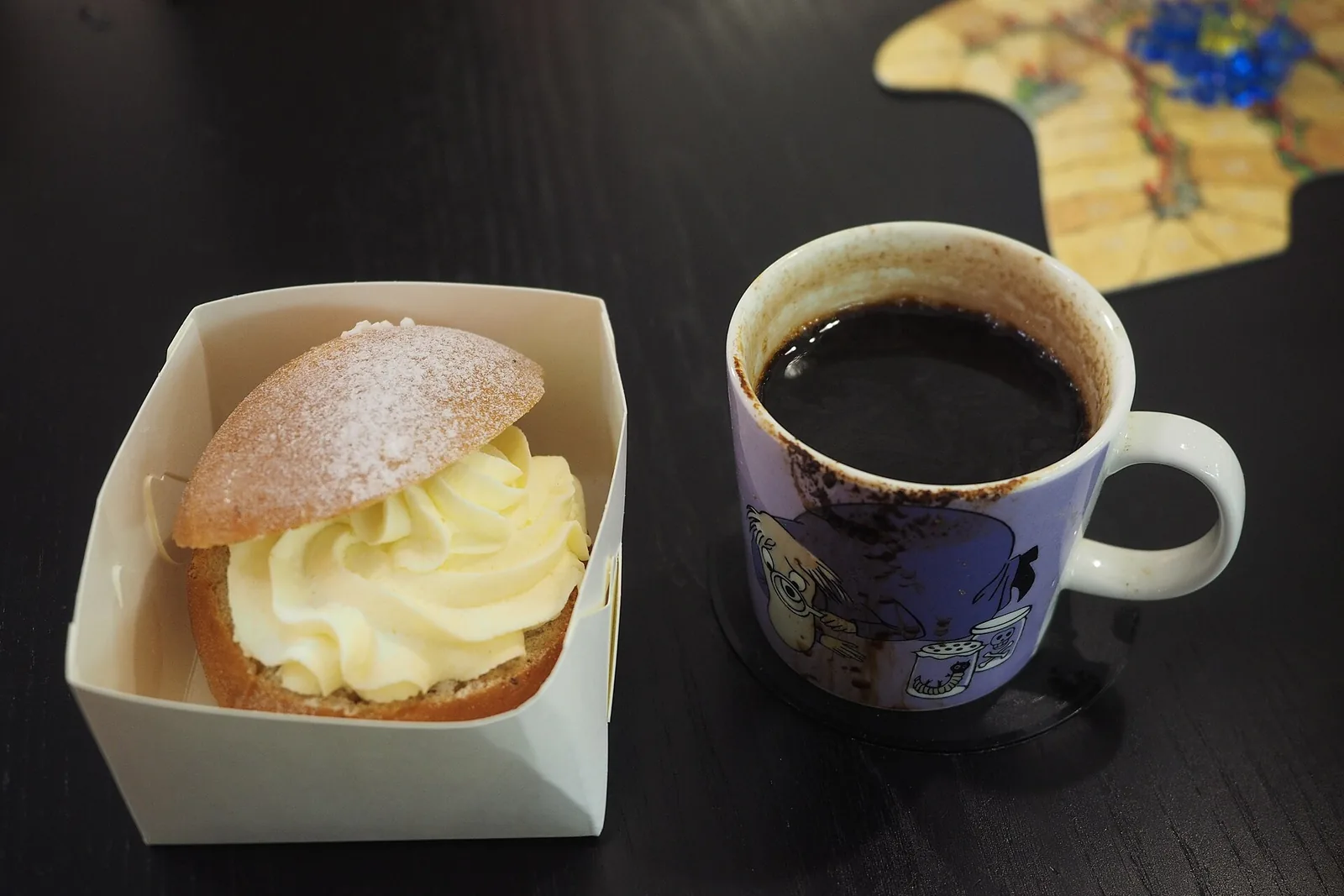 Kahvia täynnä oleva violetti muumimuki ja laskiaispulla pöydällä